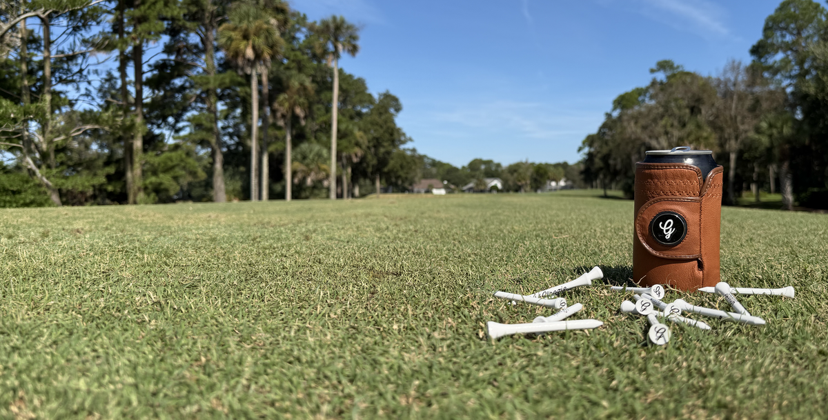 Brown Gloozie golf glove coozie on a golf course with Gloozie branded golf tees scattered on the grass nearby