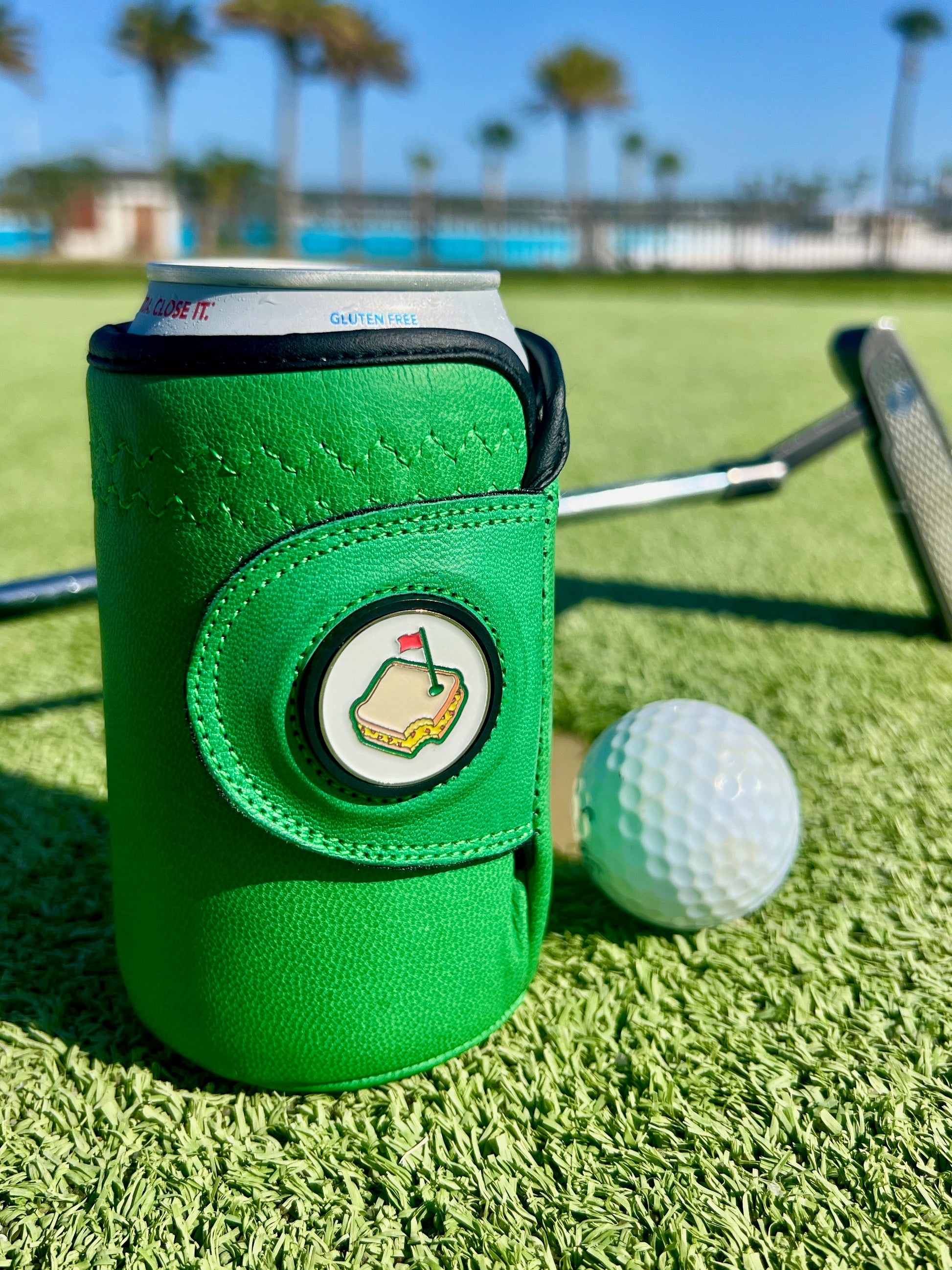 Masters green Gloozie golf glove coozie sitting on a golf course green with golf ball and putter