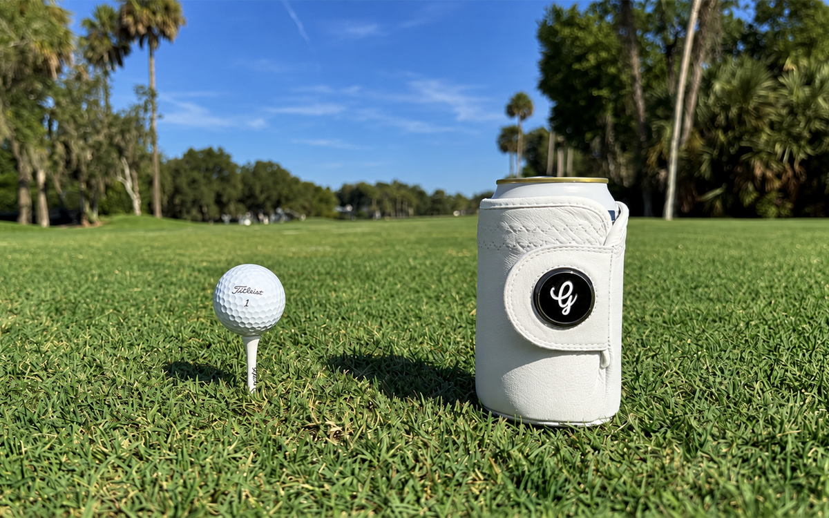 White Gloozie golf coozie beside a golf ball on a sunny golf course