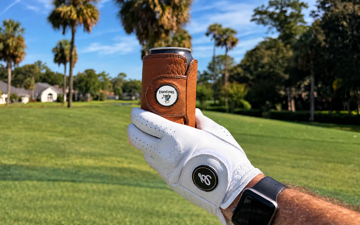 White golf glove holding a brown Gloozie golf glove coozie on a sunny golf course with Farm Links Golf Ball Marker